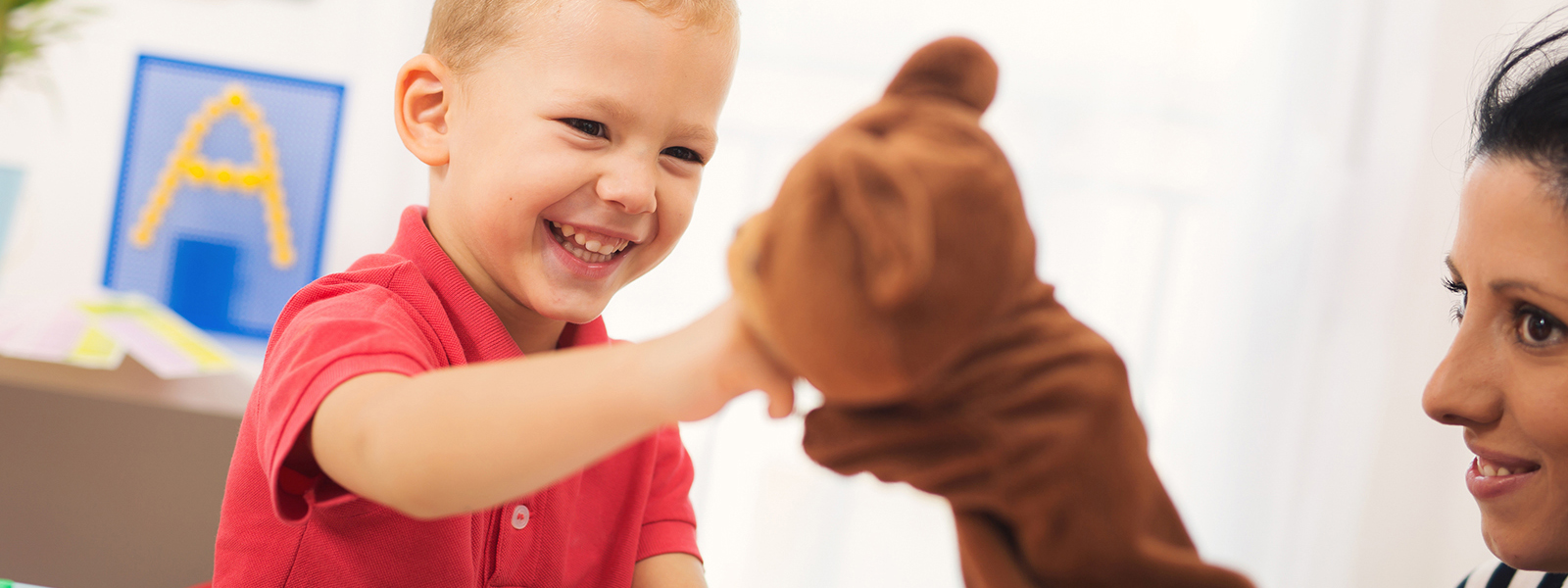 child smiling and pointing at puppet smiling teacher is using